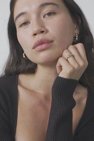 Close-up of woman wearing black long sleeve top and matching gold plated earrings and ring. 
