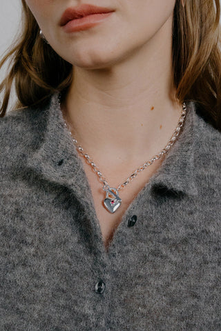 Necklace with a heart pendant worn by a person in a gray shirt.