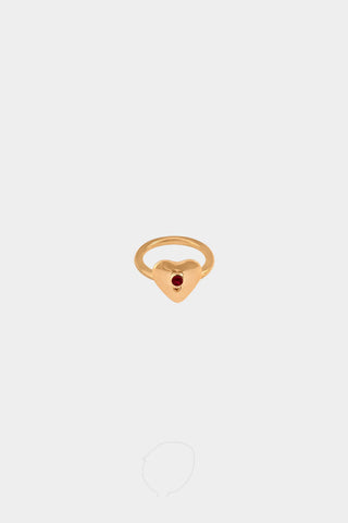A gold heart-shaped ring with a small ruby gemstone in the center, displayed on a light gray background.