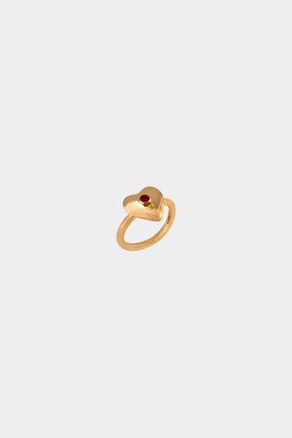 A gold heart-shaped ring with a small ruby gemstone in the center, displayed on a light gray background.