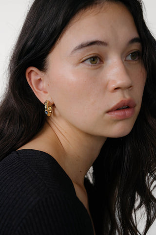 Woman wearing gold hoop earrings with 3 gemstones. 