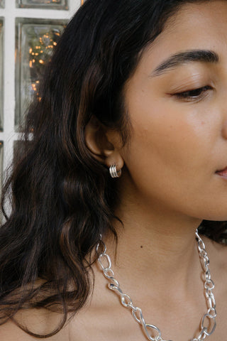 Close-up of a woman wearing silver earrings and a chain necklace.