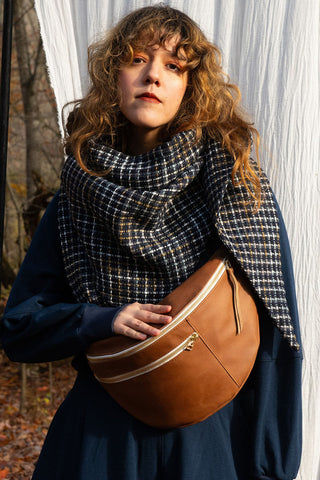 Women in front of white curtain wearing blue check scarf with brown leather bag. 