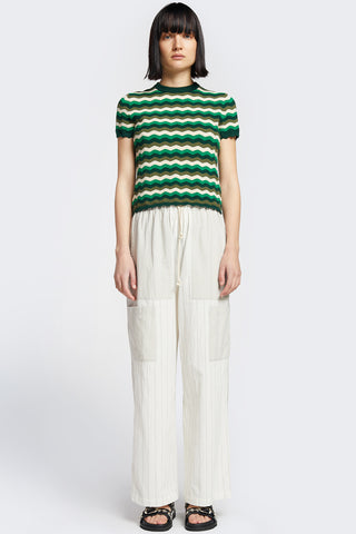 Woman wearing white pants and green wavy knit Stay knitted top by Kloke. 