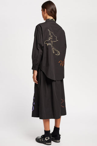 Back view of woman standing in front of white background wearing black embroidered Universe skirt and matching shirt by Kloke. 