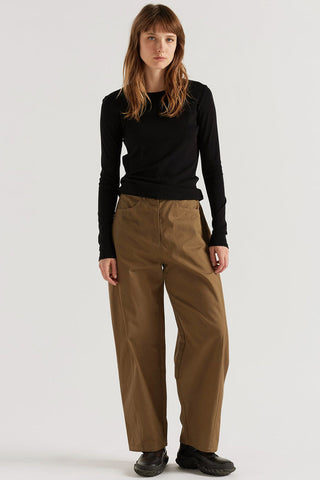A woman modeling a black long-sleeve top and wide-leg brown pants against a plain light gray studio background.