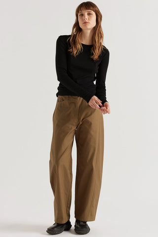 A woman modeling a black long-sleeve crewneck top and wide-leg brown pants against a plain light gray studio background.
