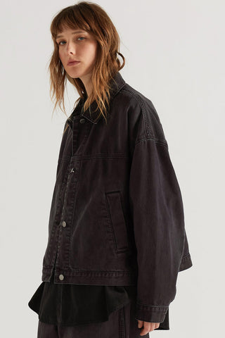 A model wearing an oversized, dark washed denim jacket, photographed against a neutral light gray studio background.