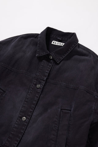 Close-up of a dark washed denim jacket with a visible KLOKE brand label on the inner neck, set against a plain light gray background.