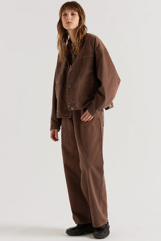 A model wearing a matching brown denim jacket and wide-leg trousers set, standing against a plain light gray studio background.
