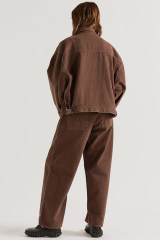 A model shown from the back wearing a matching brown oversized denim jacket and wide-leg denim pants, paired with black shoes, against a plain light gray studio background.