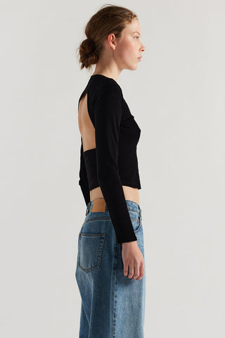 Side view of woman wearing black long sleeve open back shirt and baggy jeans. 