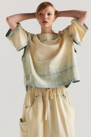 Woman wearing faded denim relaxed fit top slit detailing under the arms, with matching drawstring waist skirt. 
