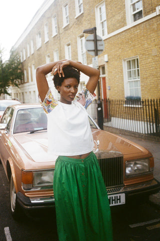 Woman standing in front of car with white t-shirt and green button up Isaac skirt by LF Markey. 