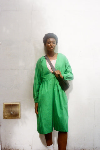 Woman standing in front of a wall wearing a knee length green Warren dress by LF Markey. 