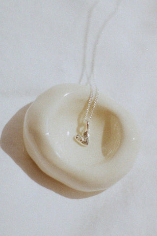 Sterling silver heart shaped pendant on chain on ivory ceramic bowl. 