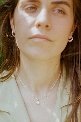 Close-up of woman wearing light green shirt, silver earrings and shell pendant necklace. 