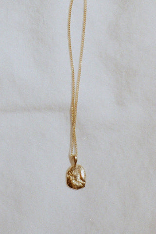 Gold textured pendant on gold chain in front of white background. 