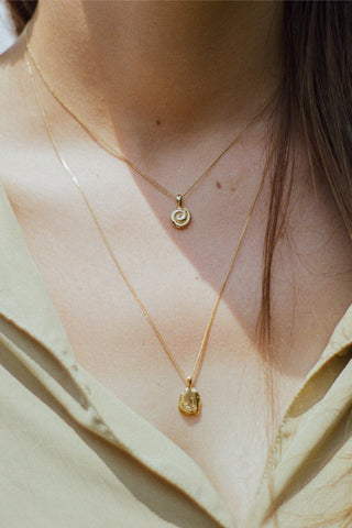 Close-up of woman wearing gold shell pendant necklace and textured gold pebble pendant necklace with light green blouse. 