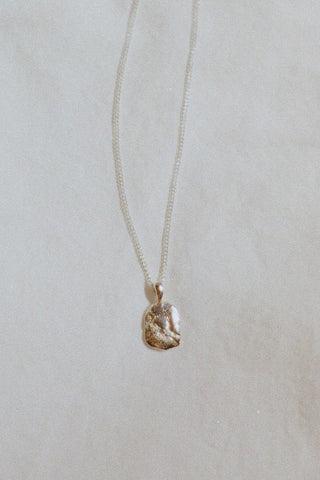 Silver textured pendant on silver chain in front of white background. 