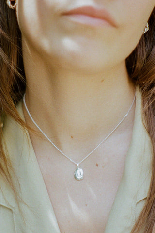 Close-up of woman wearing textured silver pebble pendant necklace with light green blouse. 