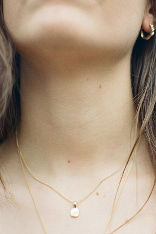 Close-up of woman's neck earing gold pebble pendant necklace. 