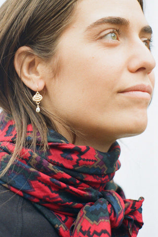 Woman wearing multi colour scarf and gold hook earring with dangling pearl. 