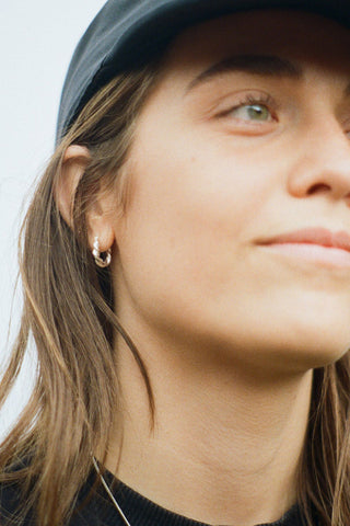 Close-up of woman wearing black hat and silver braided sleeper hoop earrings. 