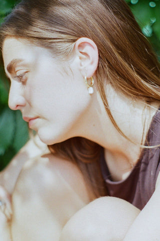 Side profile of woman wearing gold vermeil sleeper earrings with dangling pearl. 