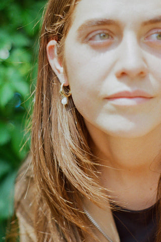 Close-up of woman wearing gold vermeil sleeper earrings with dangling pearl. 