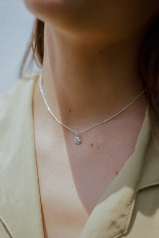 Close-up of woman wearing light green shirt and silver shell pendant necklace. 