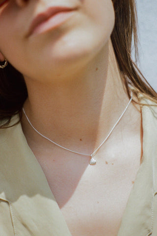 Close-up of woman wearing light green shirt and silver shell pendant necklace. 