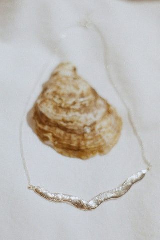 Sterling silver wavy necklace with blurry oyster shell on white backdrop. 