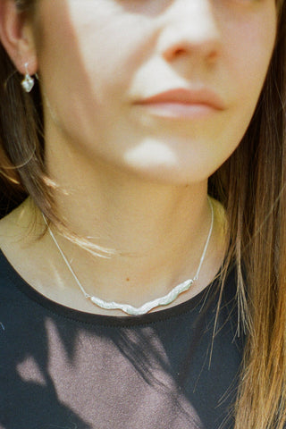 Close-up of woman wearing wavy sterling silver necklace and black top. 