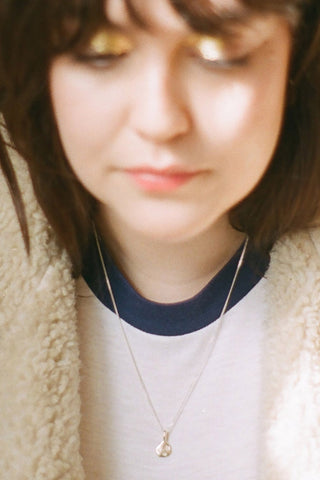 Blurry close-up photo of a woman wearing sterling silver Prairie necklace by La Manufacture Fait Main Prairie. 