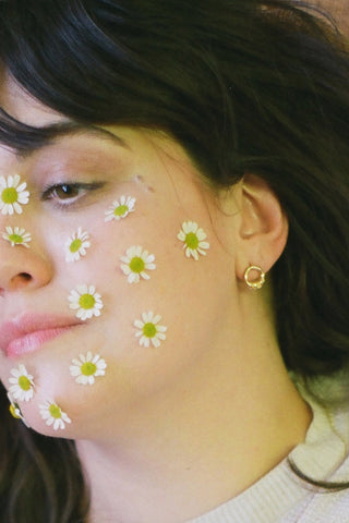 Woman with flowers on her face wearing gold vermeil Ombelle stud earrings by La Manufacture Fait Main. 