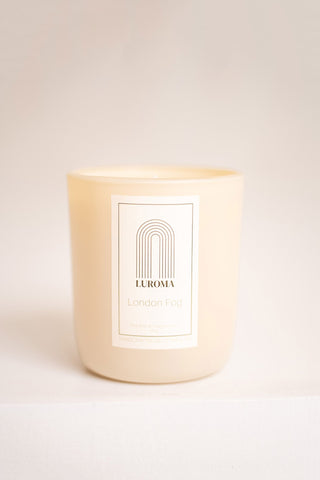 Candle in beige glass container with white label that reads "Luroma - London Fog". Photographed in front of beige background. 