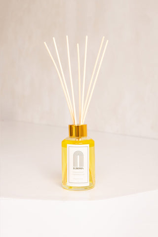 A glass jar and wood reed diffuser with white label that reads "Laroma". 