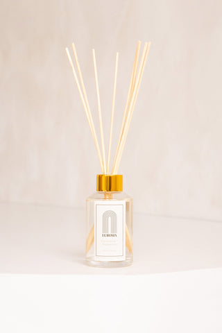 A glass jar and wood reed diffuser with white label that reads "Laroma". 