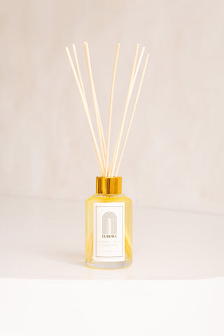 A glass jar and wood reed diffuser with white label that reads "Laroma". 