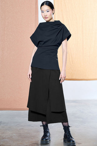 Women wearing navy asymmetrical shirt with black cropped pants with asymmetrical draped panel, styled with black boots. 