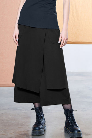 Waist down photo of a woman wearing a navy top and black cropped pants with asymmetric front panel, paired with black Dr. Martens. 