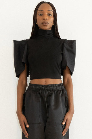 Woman wearing black turtleneck top with structured sleeves and black pants. 