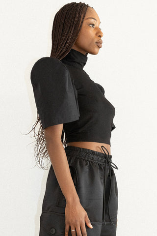 Side view of woman wearing black turtleneck top with structured sleeves and black pants. 