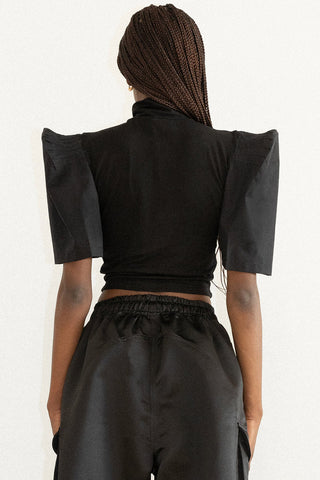 Back view of woman wearing black turtleneck top with structured sleeves and black pants. 