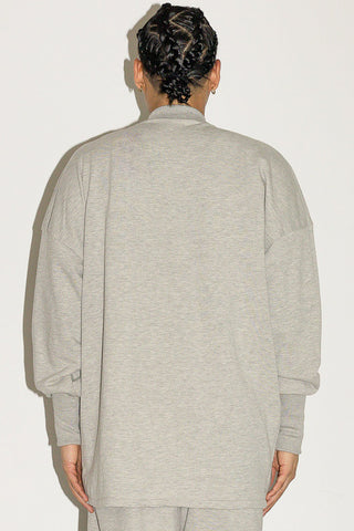 Back view of man in front of white background wearing grey sweater. 