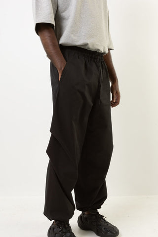 A person wearing black pants with an elastic waistband and side pockets, paired with a light gray t-shirt and black sneakers, photographed against a plain white studio background.
