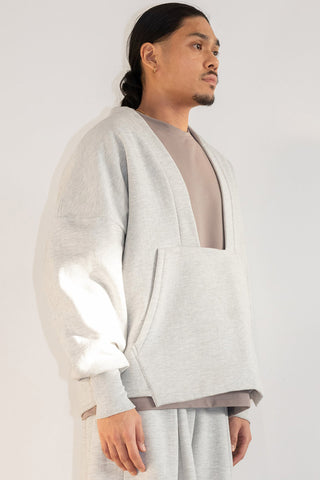 Side view of man in front of white background wearing light grey oversized shawl collar sweater. 