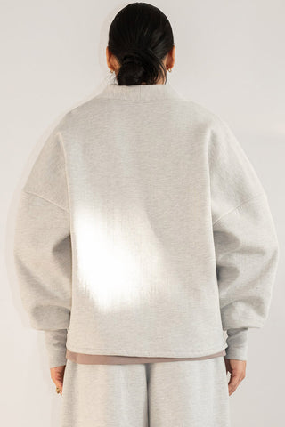 Back view of man in front of white background wearing light grey oversized shawl collar sweater. 