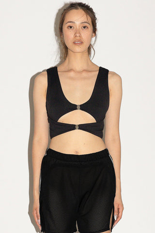 Woman in front of white background wearing a black tank top with cut-out detail and black mesh shorts. 